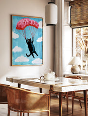 Whimsical illustration of a black cat descending with a pink floral parachute in a blue sky with, in a styled room mockup