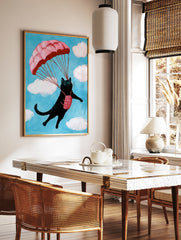 A whimsical illustration of a black cat parachuting with a pink parachute against a blue sky with, in a styled room mockup