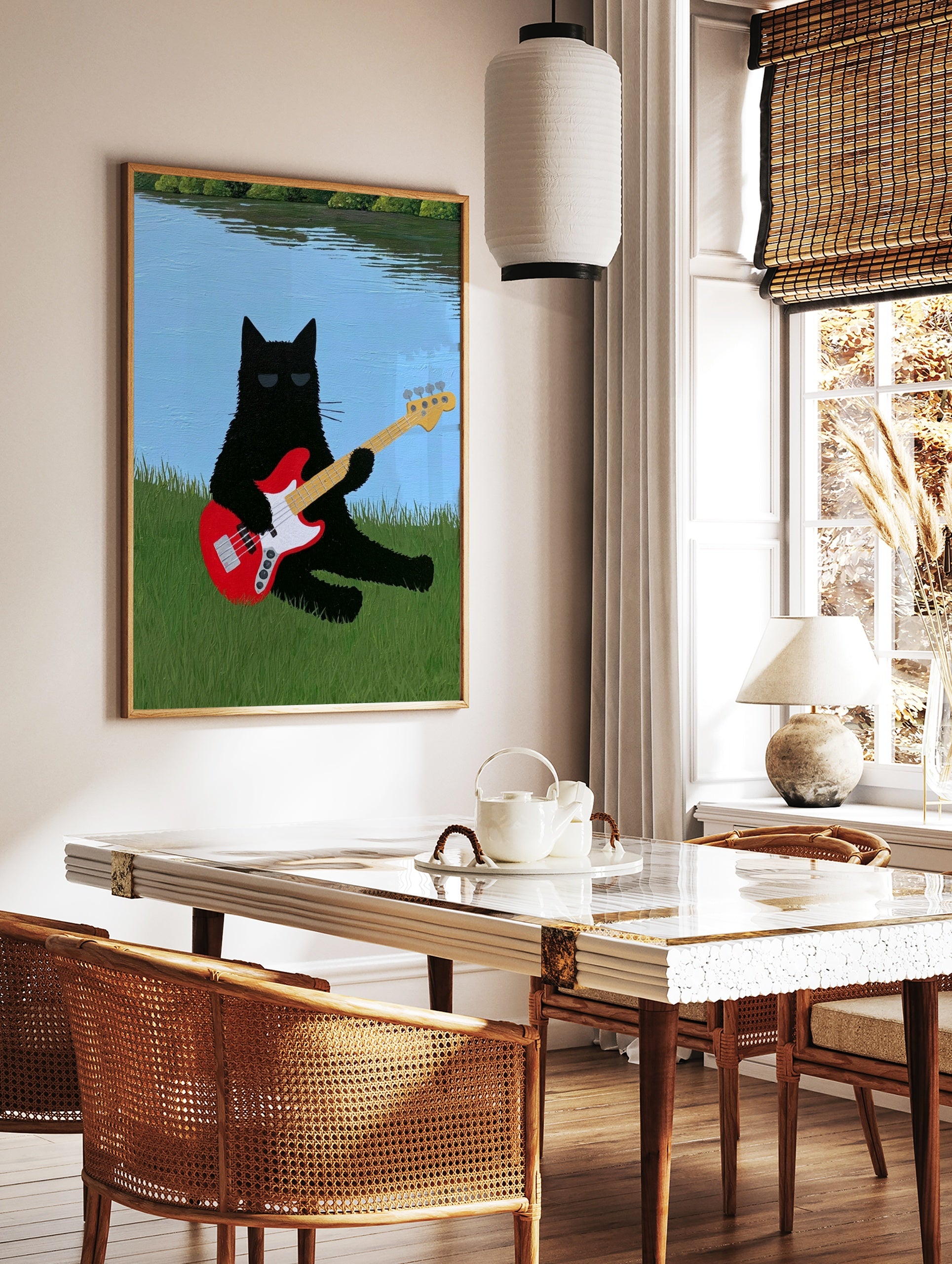 Black cat with sunglasses playing a red bass guitar in green grass by a blue lake illustrative wall, in a styled room mockup
