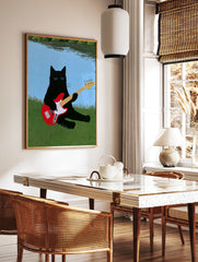 Black cat with sunglasses playing a red bass guitar in green grass by a blue lake illustrative wall, in a styled room mockup