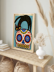 Stylized black cat standing on a decorative Mexican sugar skull with blue, red, and yellow, in an alternate framed mockup