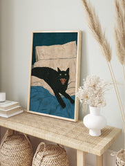 Black cat with green eyes and open mouth hissing on a bed with blue blanket and beige pillow, in an alternate framed mockup