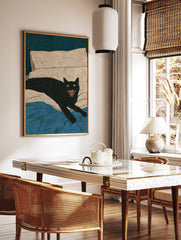 Black cat with green eyes and open mouth hissing on a bed with blue blanket and beige pillow, in a styled room mockup