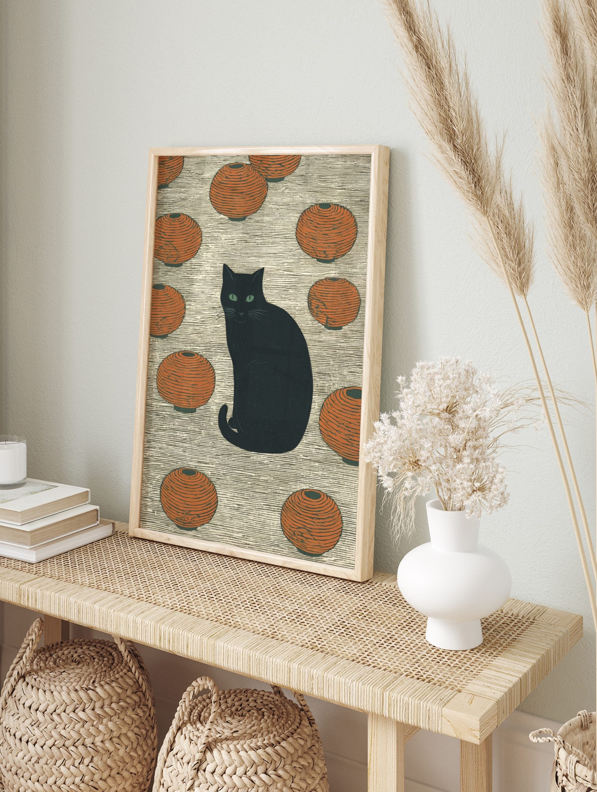 Black cat with green eyes sitting among orange Japanese lanterns on a textured background, in an alternate framed mockup