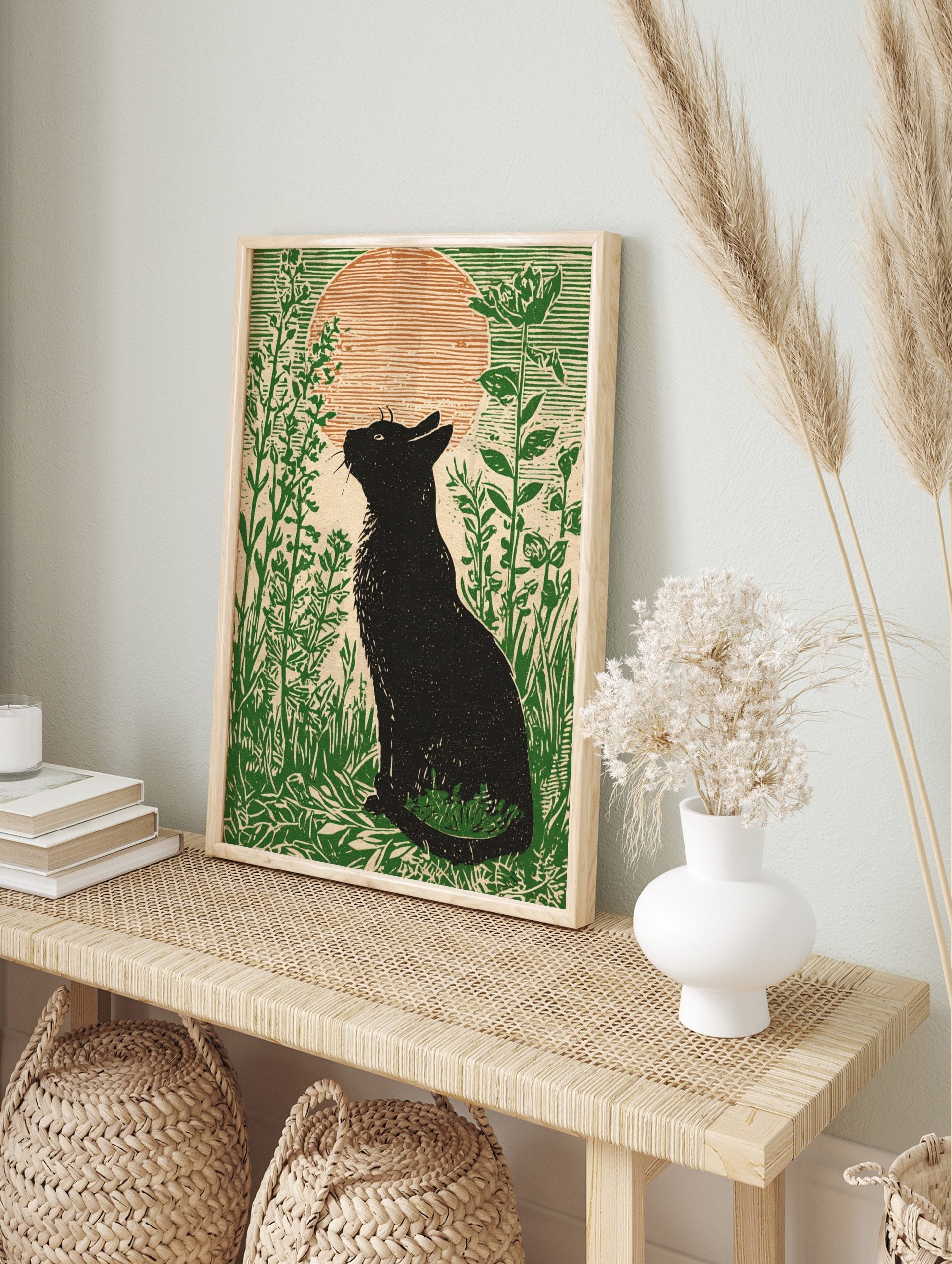 Black cat silhouette looking at a large orange moon in a field of green plants, illustrative, in an alternate framed mockup