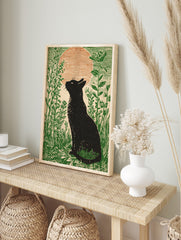 Black cat silhouette looking at a large orange moon in a field of green plants, illustrative, in an alternate framed mockup