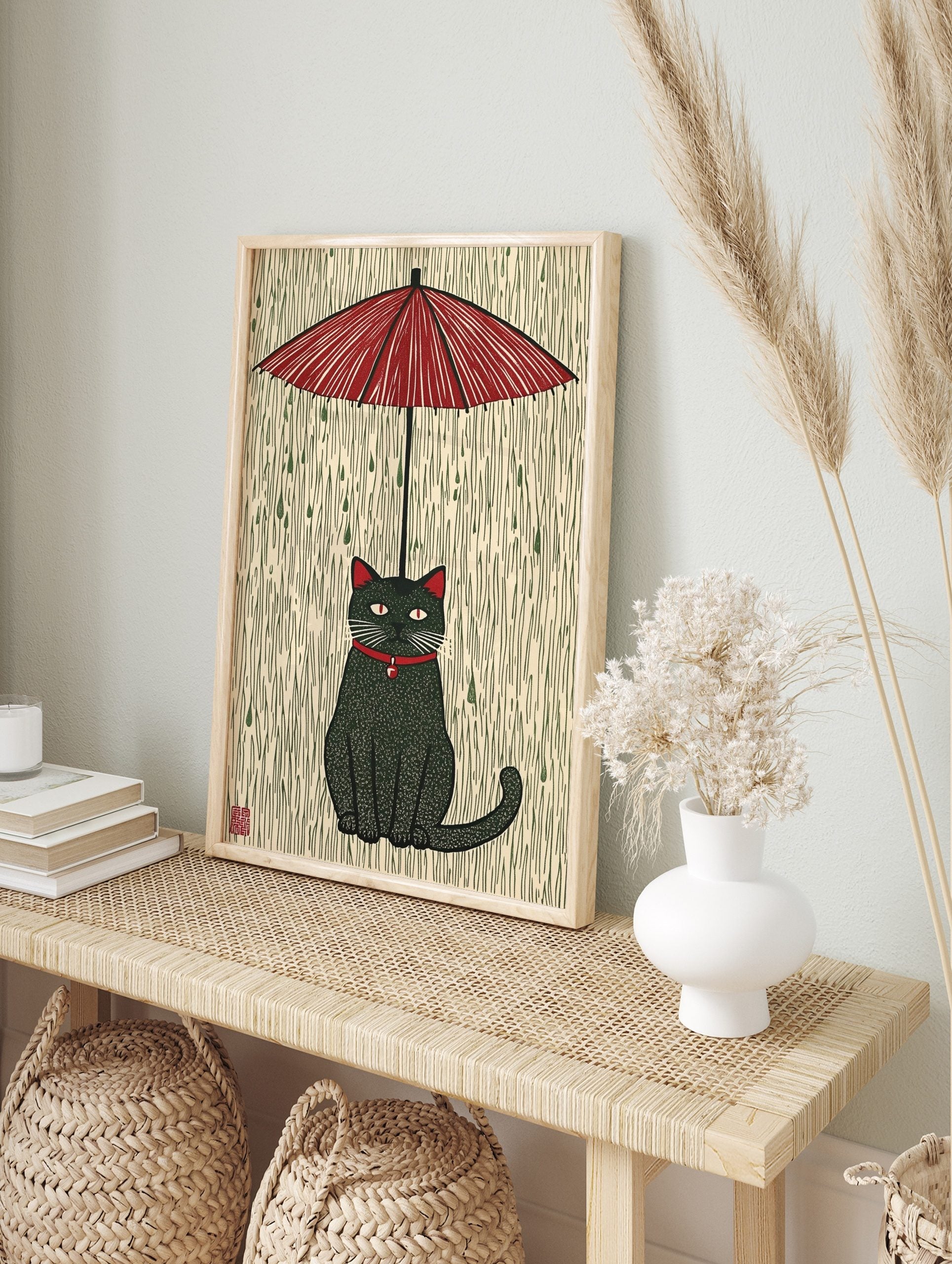 Stylised black cat with red collar and eyes sitting under a red umbrella in green rain, in an alternate framed mockup