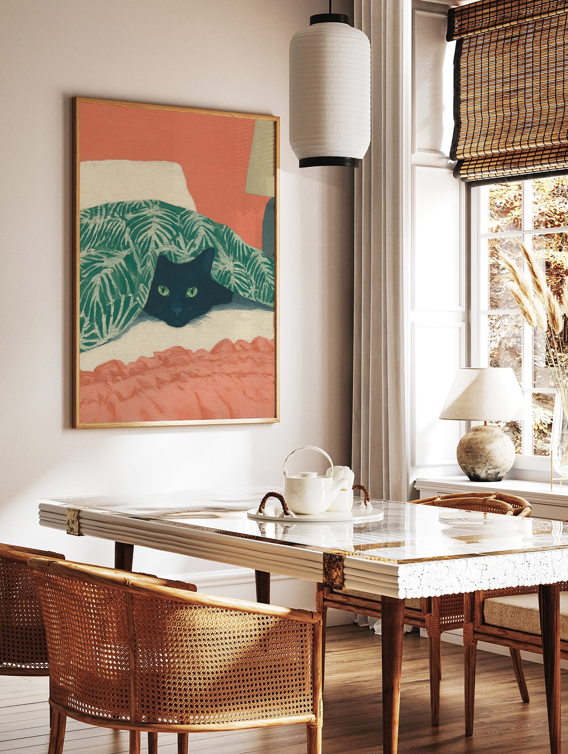 Illustrative print of a black cat with green eyes peeking from under a green tropical leaf blanket, in a styled room mockup