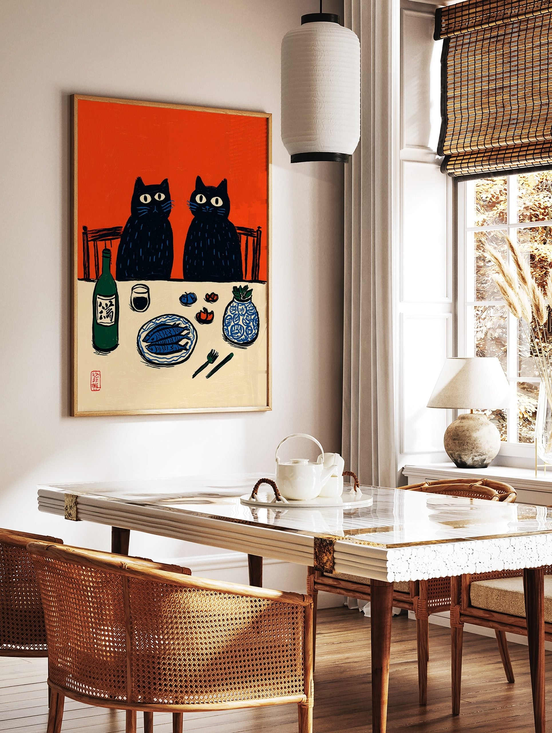 Illustrative print of two black cats at a dinner table with fish, sake, and a vase, against an, in a styled room mockup