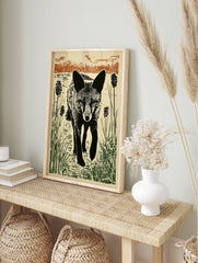 Black fox linocut print walking through green and brown reeds with an intense gaze, in an alternate framed mockup