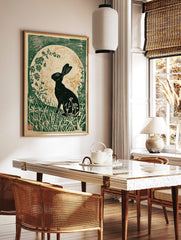 Black hare silhouette against a textured moon, surrounded by green foliage in an illustrative print, in a styled room mockup