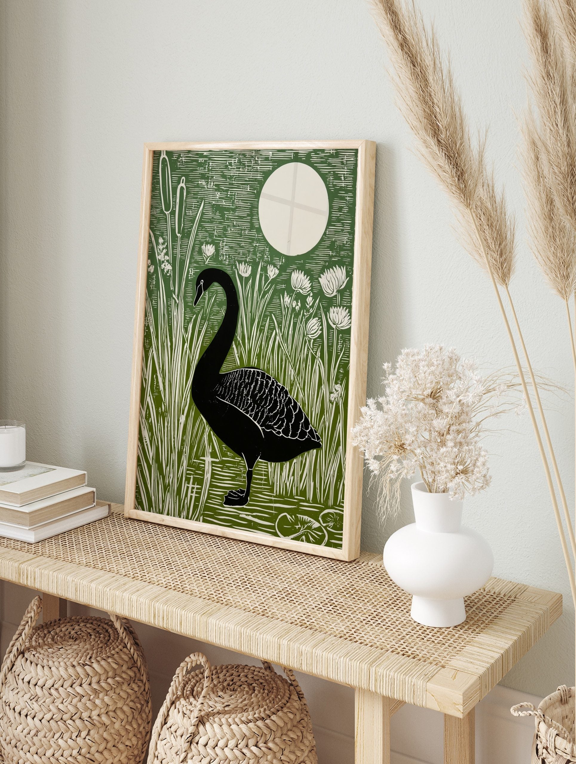 Black swan standing in water surrounded by green cattails and white flowers, with a large, in an alternate framed mockup