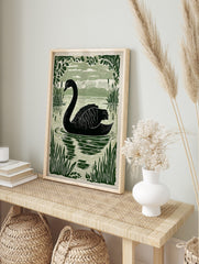 Black swan swimming in a lake, surrounded by green reeds and leafy branches in an, in an alternate framed mockup