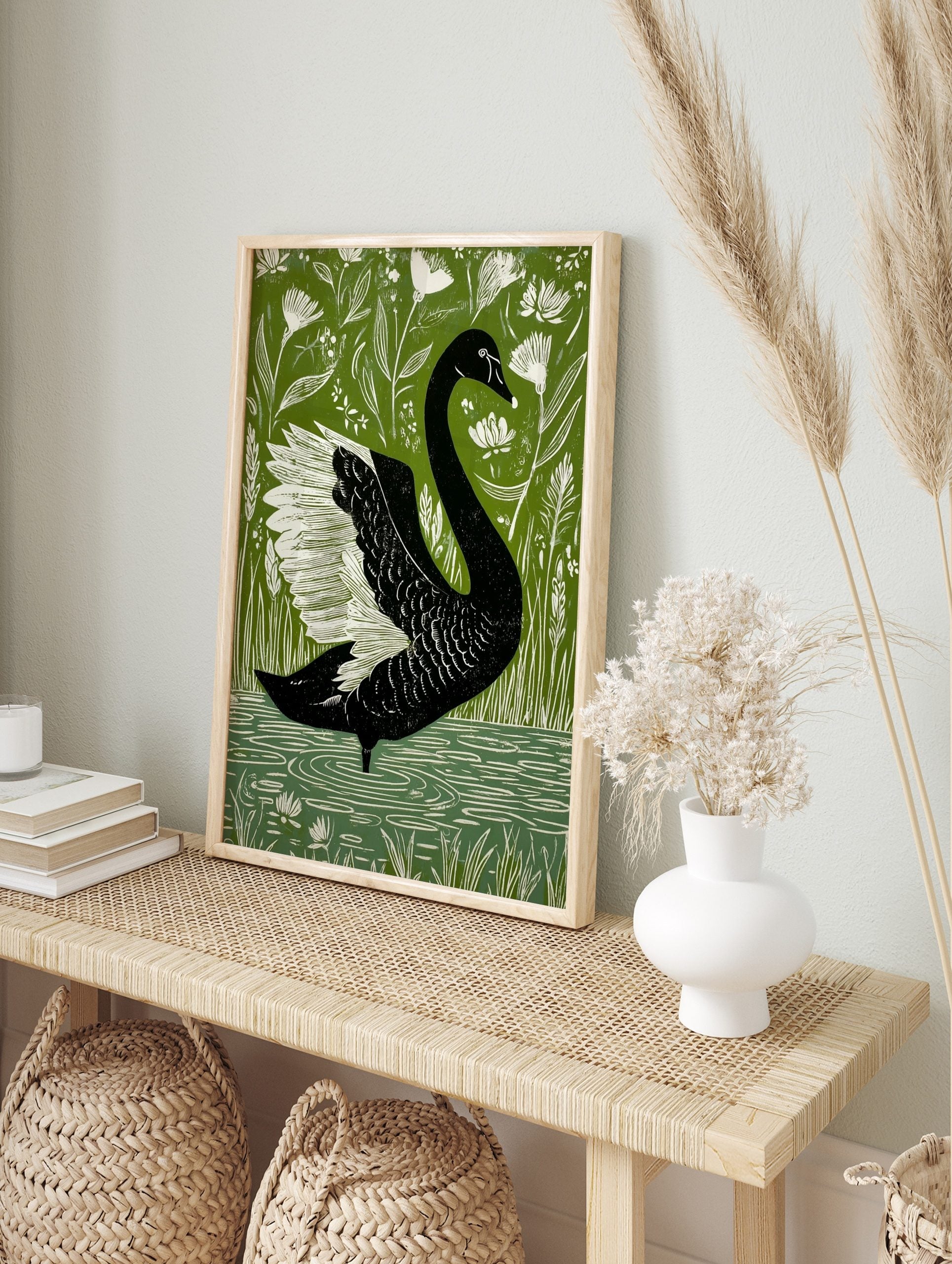 Black swan with white wings in a bold illustrative style, surrounded by green foliage and, in an alternate framed mockup