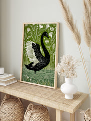 Illustrative black swan with white wings on green background with white botanical plants and, in an alternate framed mockup