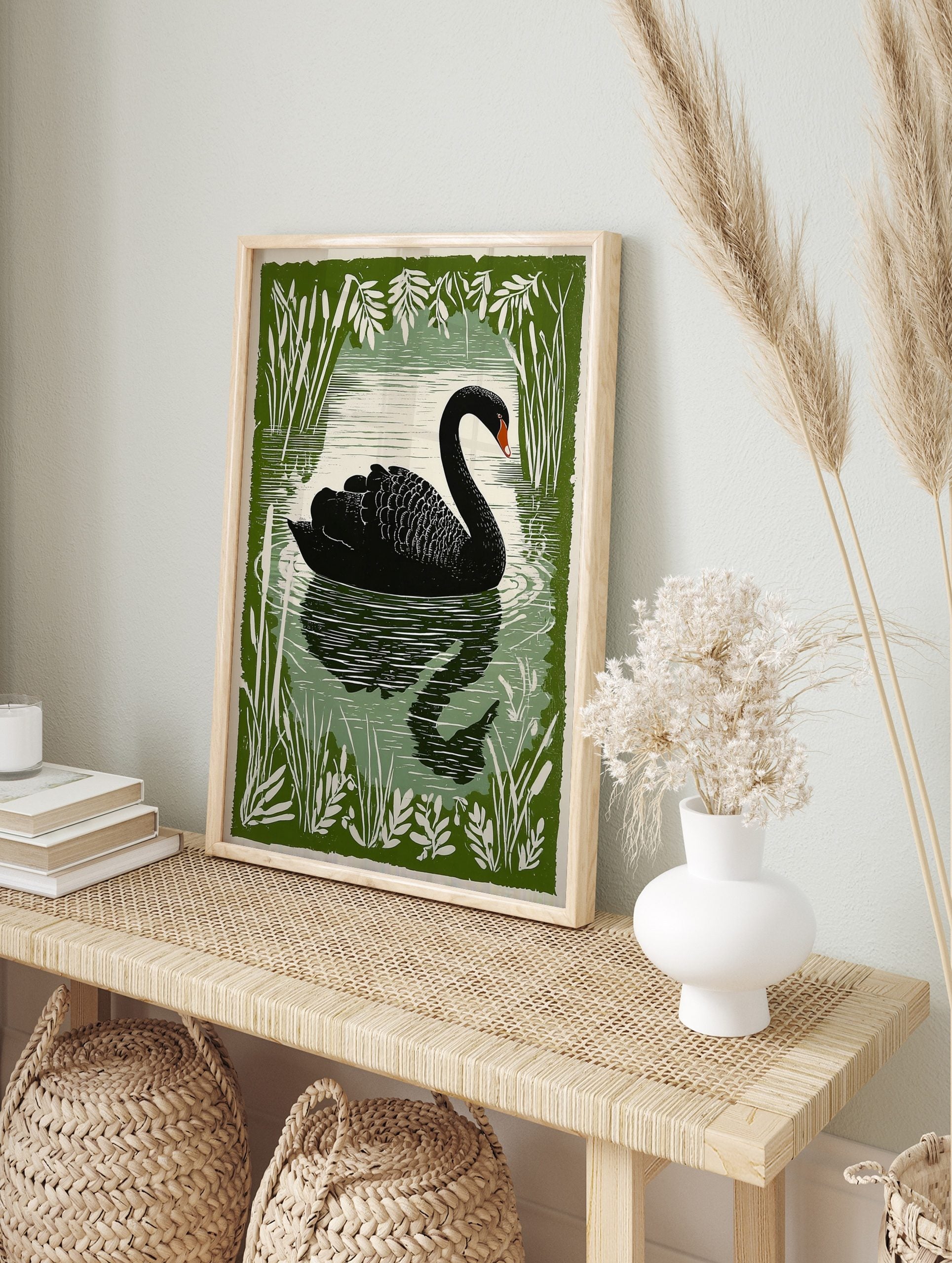 Illustrative black swan swimming on water, framed by green cattails and leaves, with a, in an alternate framed mockup