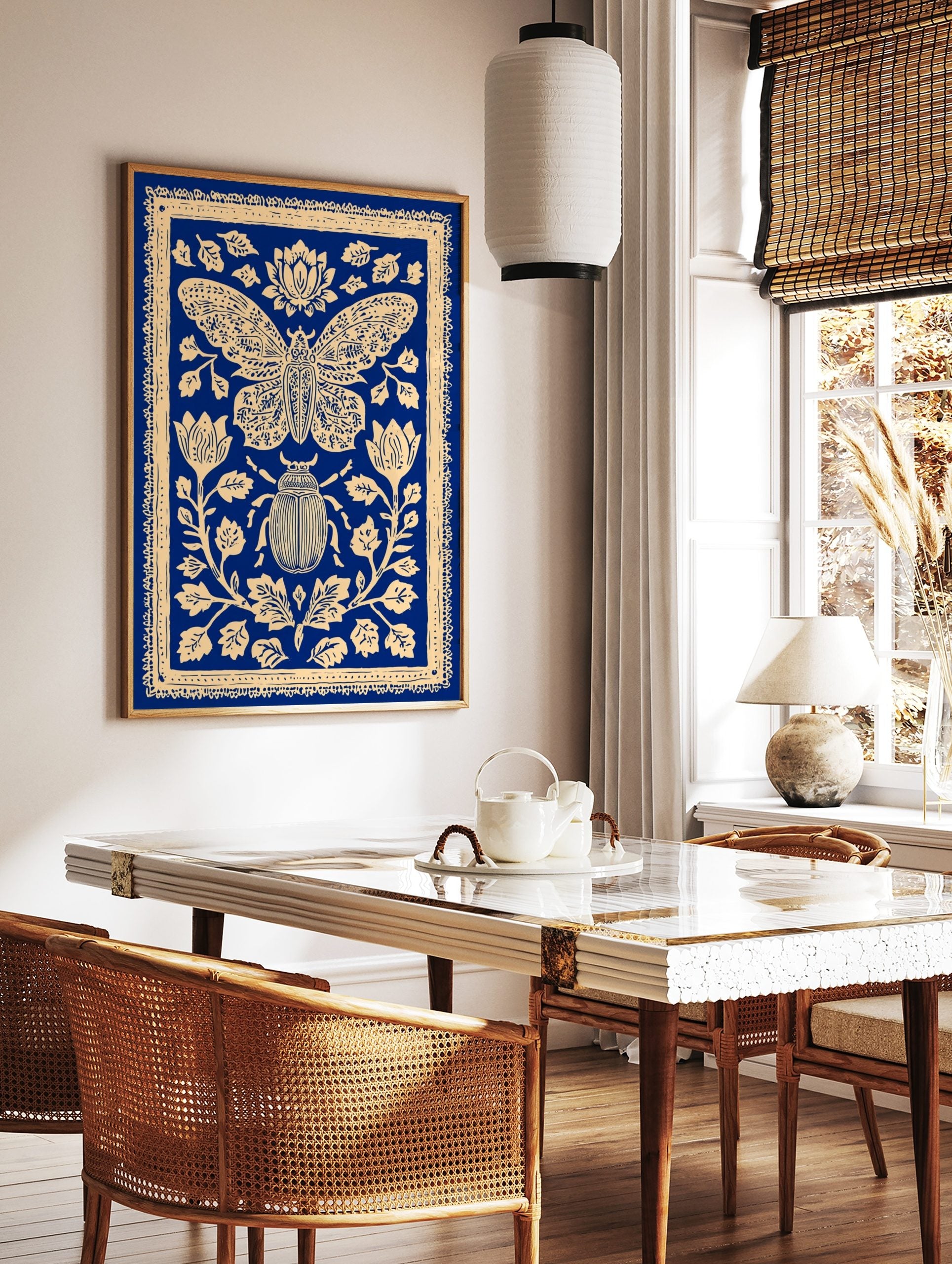 Blue and cream illustrative print of a moth and beetle surrounded by ornate botanical flowers and, in a styled room mockup