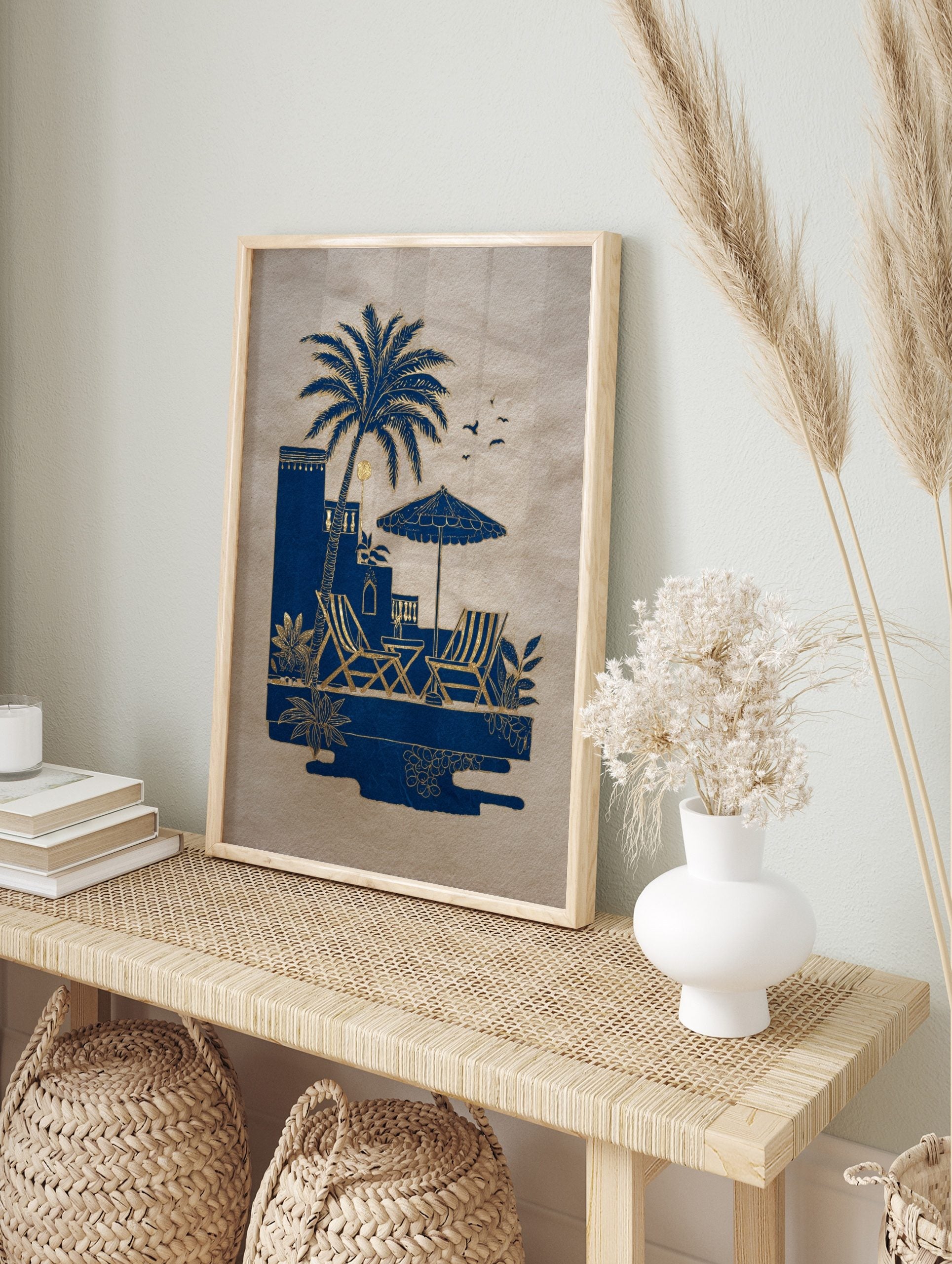 Blue and gold illustrative art print of a palm tree, deck chairs, and parasol by a pool on, in an alternate framed mockup
