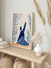 Illustrative print of a woman in a blue outfit in a kneeling yoga pose, reaching for blue, in an alternate framed mockup