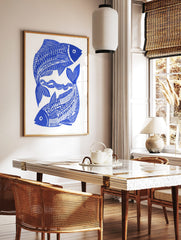 Blue and white illustrative print of two stylised fish intertwined with wavy lines on a white, in a styled room mockup