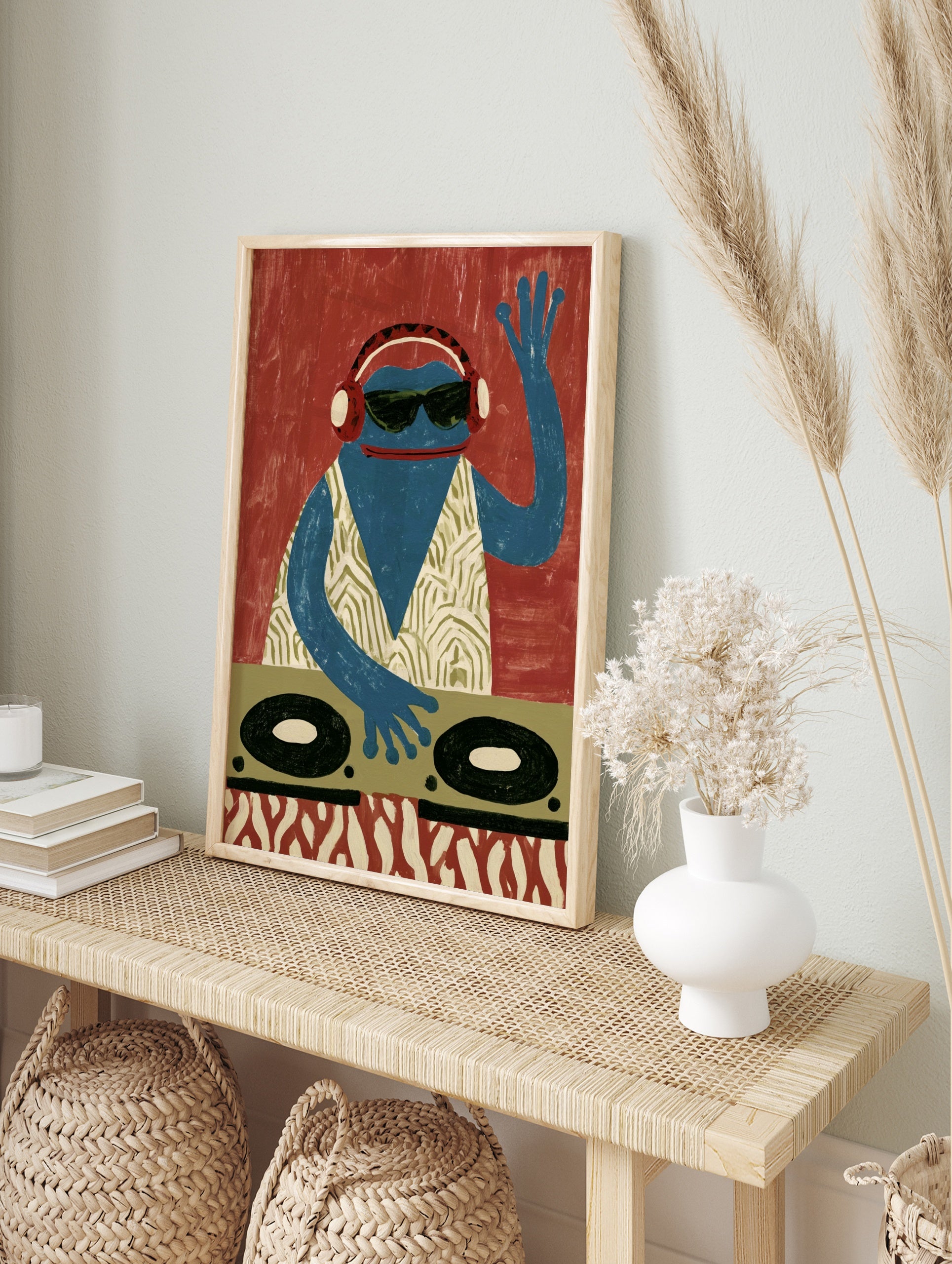 A blue frog DJ wearing headphones and sunglasses behind turntables, graphic illustrative wall, in an alternate framed mockup