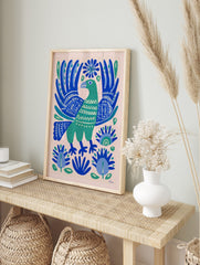 Green folk art bird with ornate blue wings and botanical patterns on a light background, in an alternate framed mockup
