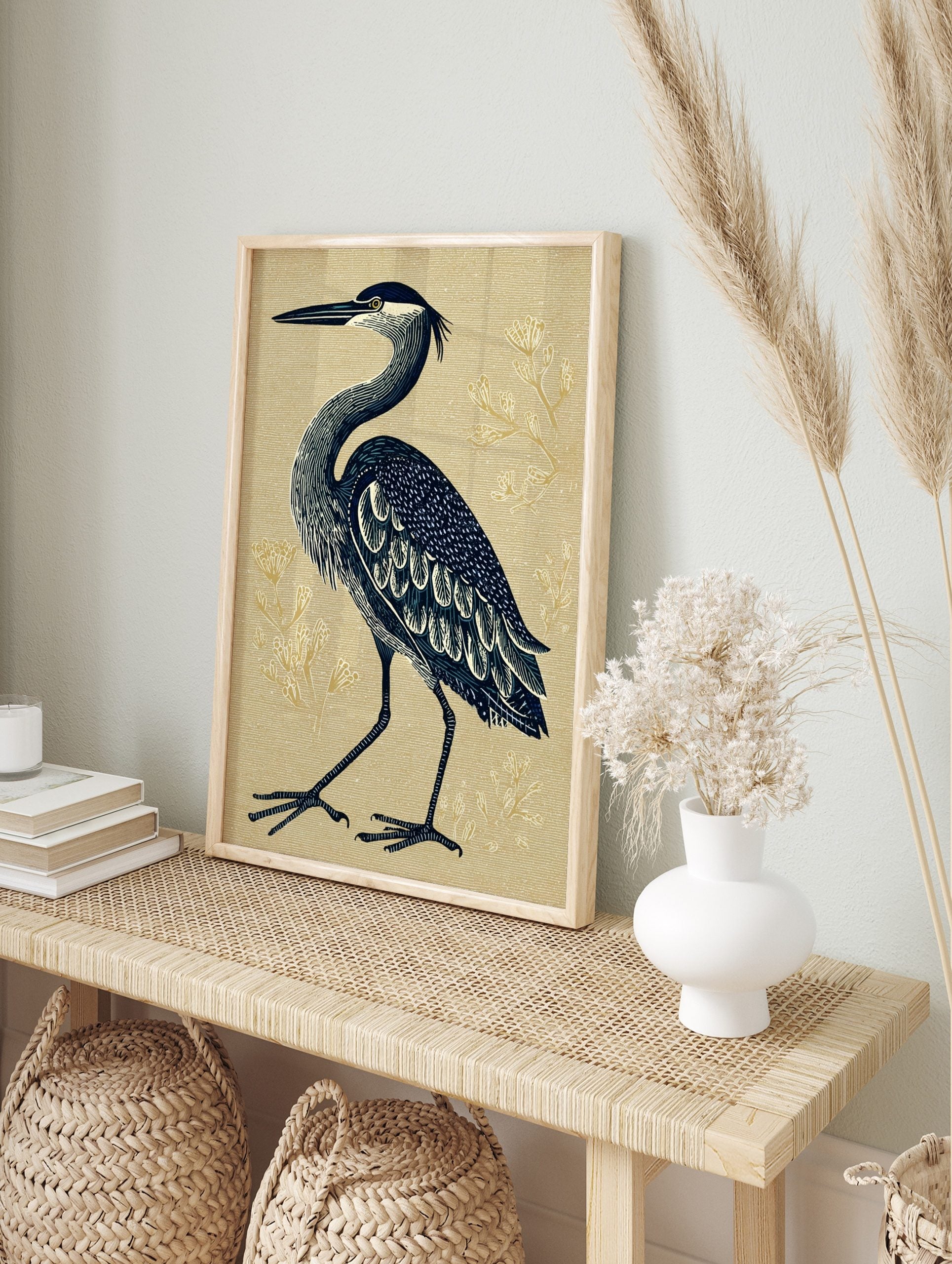 Illustrative blue heron standing on a textured beige background with subtle gold botanical, in an alternate framed mockup