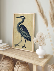 Illustrative blue heron standing on a textured beige background with subtle gold botanical, in an alternate framed mockup