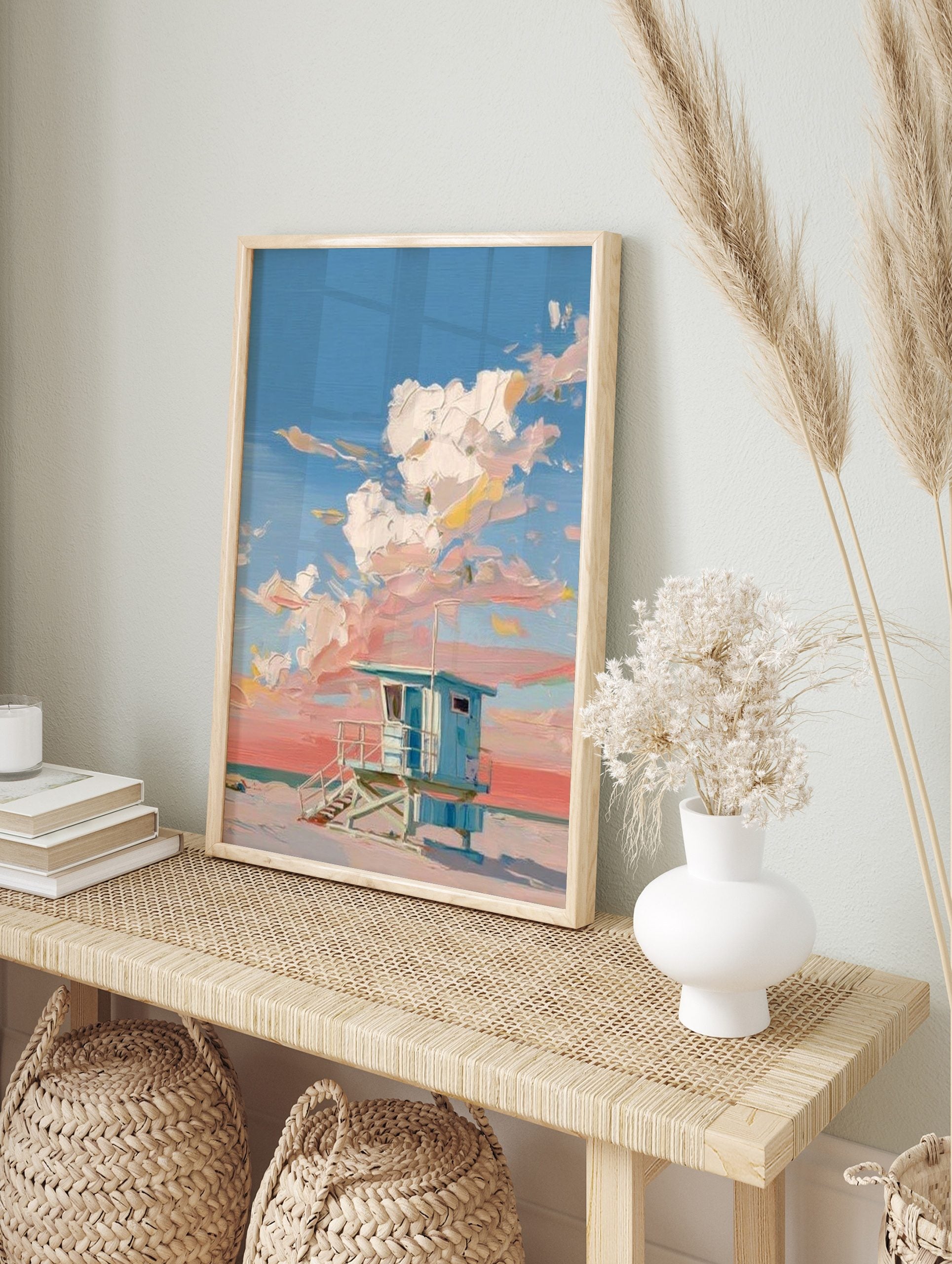 Blue lifeguard hut on a sandy beach with thick impasto clouds in a pink and blue sky, in an alternate framed mockup