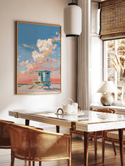 Blue lifeguard hut on a sandy beach with thick impasto clouds in a pink and blue sky, in a styled room mockup
