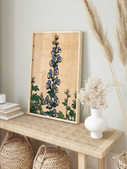 Vintage botanical illustration of blue monkshood flowers with green leaves on a tan background, in an alternate framed mockup
