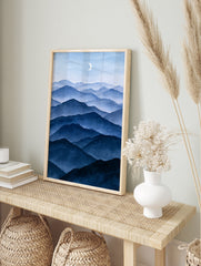 Minimalist blue mountain landscape illustration with layered peaks and a crescent moon, in an alternate framed mockup