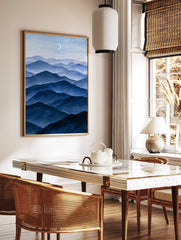 Minimalist blue mountain landscape illustration with layered peaks and a crescent moon, vertical, in a styled room mockup