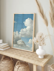 Close-up of a painting depicting a vast blue sky filled with large, fluffy white and grey, in an alternate framed mockup