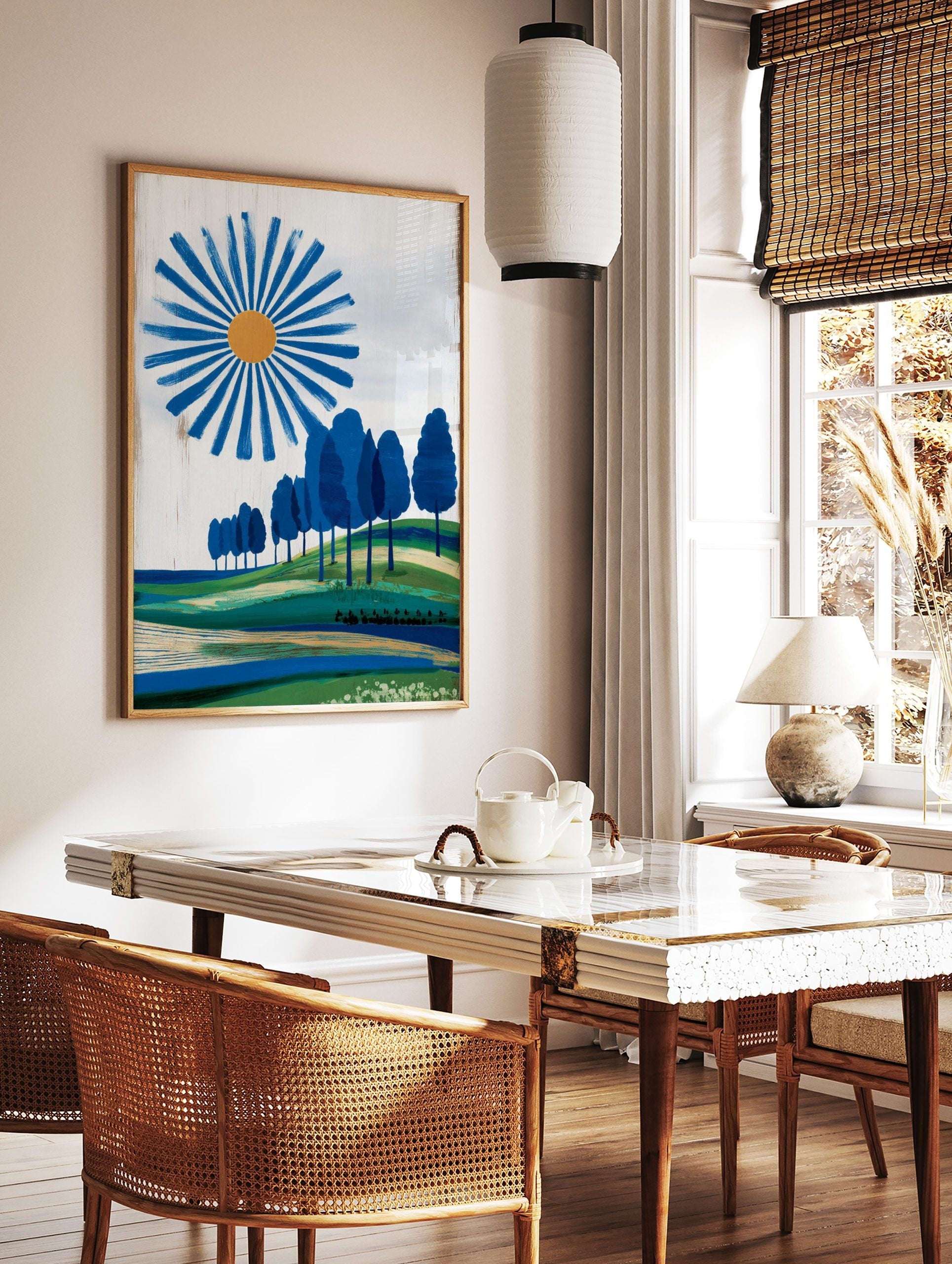 Modern landscape print with a blue sun, orange centre, radiating blue brushstrokes, green hills, in a styled room mockup