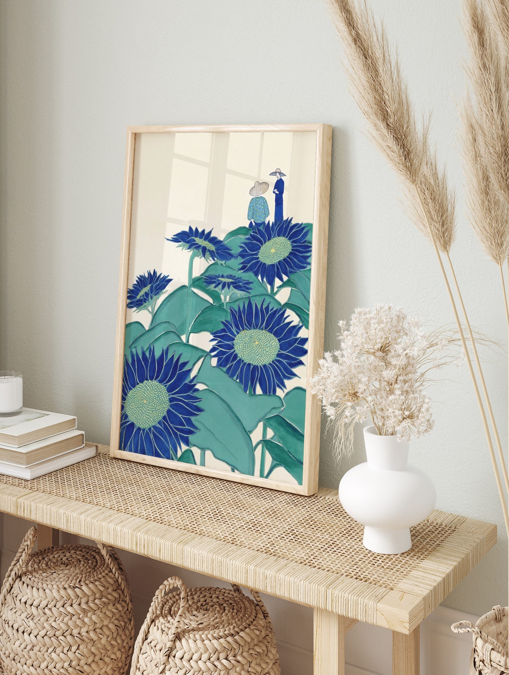 Illustrative blue sunflowers with green leaves and two figures in hats on a cream background, in an alternate framed mockup