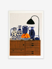 Still life art print featuring four patterned blue and white vases, a bowl of oranges, and a desk lamp on a wooden cabinet