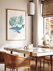 Watercolour illustration of a blue whale with white spots swimming below two clusters of teal, in a styled room mockup