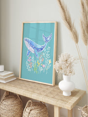 Illustrative blue whale art print with pink accents, swimming above colourful underwater, in an alternate framed mockup