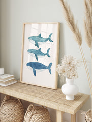 Three blue watercolour whales swimming horizontally on a light background, arranged vertically, in an alternate framed mockup