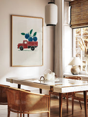 Red vintage pickup truck carrying a branch of blue blueberries and green leaves, illustrative print, in a styled room mockup
