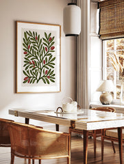 Botanical illustration print of green leafy branches with red berries on a cream background, in a styled room mockup