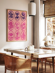 Vintage-style grid of nine botanical flower illustrations in oval frames on a pink background, in a styled room mockup