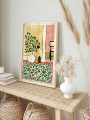 Botanical interior scene wall art print with a white vase of green and purple flowers, orange and green bottles, and a floral patterned rug. - Image 3