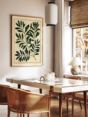Botanical leaf print with deep green foliage and thin orange border on cream paper background, in a styled room mockup