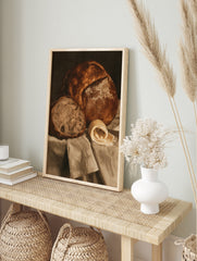 Still life wall art print of a crusty loaf of bread, a slice, and a curl of butter on draped, in an alternate framed mockup