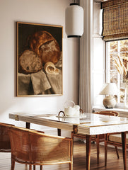 Still life wall art print of a crusty loaf of bread, a slice, and a curl of butter on draped fabric, in a styled room mockup