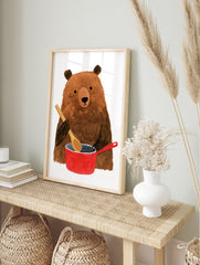 Brown bear holding a wooden spoon while cooking in a red pot illustration wall art print, in an alternate framed mockup