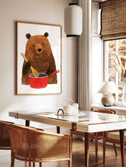 Brown bear holding a wooden spoon while cooking in a red pot illustration wall art print, in a styled room mockup