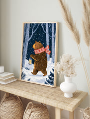 Illustrative print of a brown bear with a red scarf and lantern in a snowy forest at night, in an alternate framed mockup